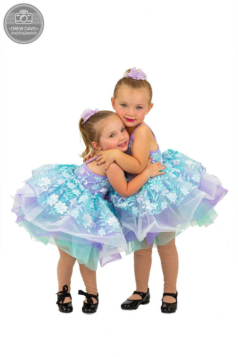 Two little dancers in matching floral tutus hugging in their recital costumes