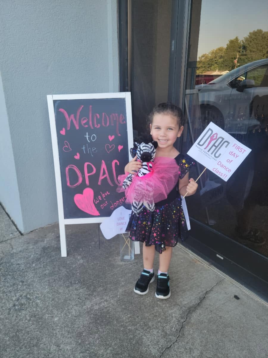 A little dancer with her first-day sign beside the Welcome to the DPAC chalkboard