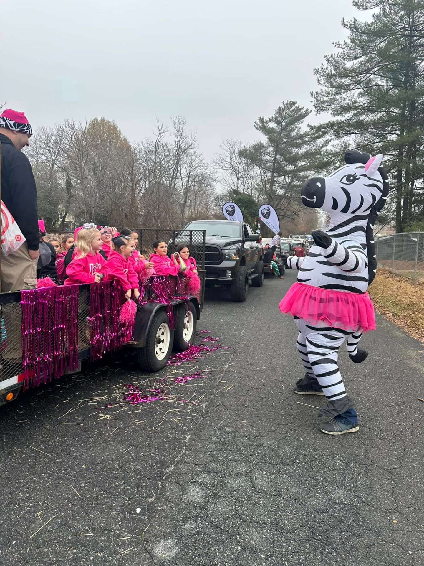 Pinky the zebra mascot in a pink tutu dancing beside the Dance Perfections parade float full of young dancers