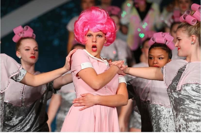 Senior dancers in pink recital costumes performing together on stage