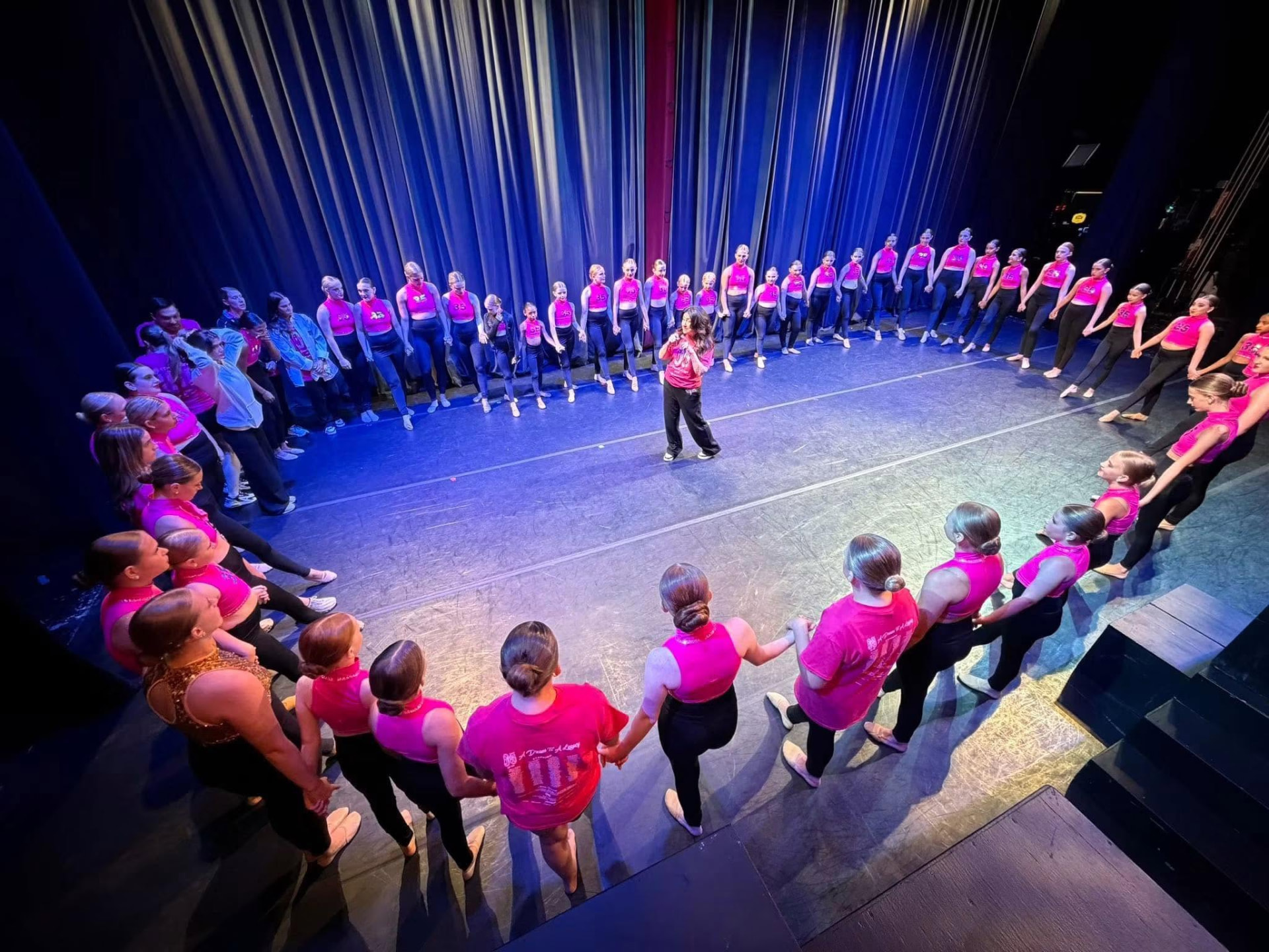 Dance Perfections dancers holding hands in a circle on stage with Michelle Brooks Webb