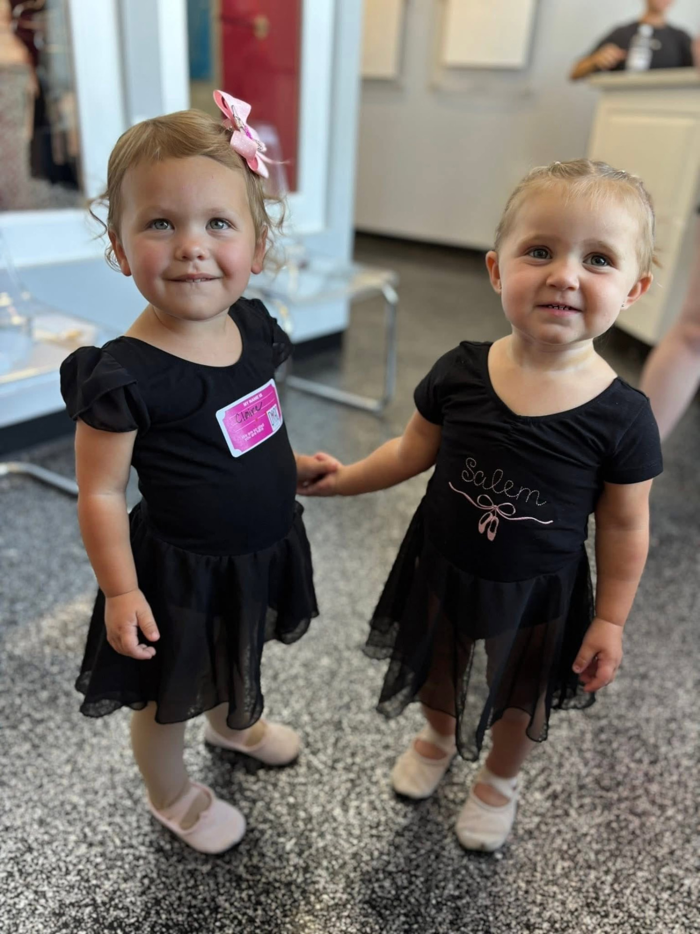 Two toddler ballerinas in black leotards holding hands before class